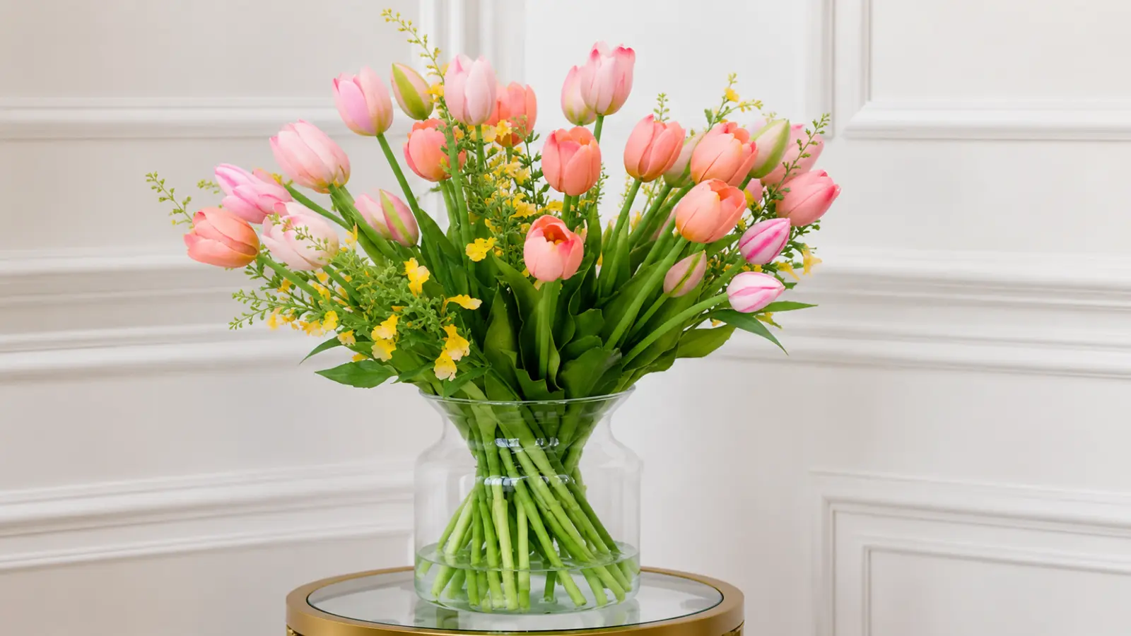 Glass vase filled with pink and peach tulips accented with delicate yellow spring flowers