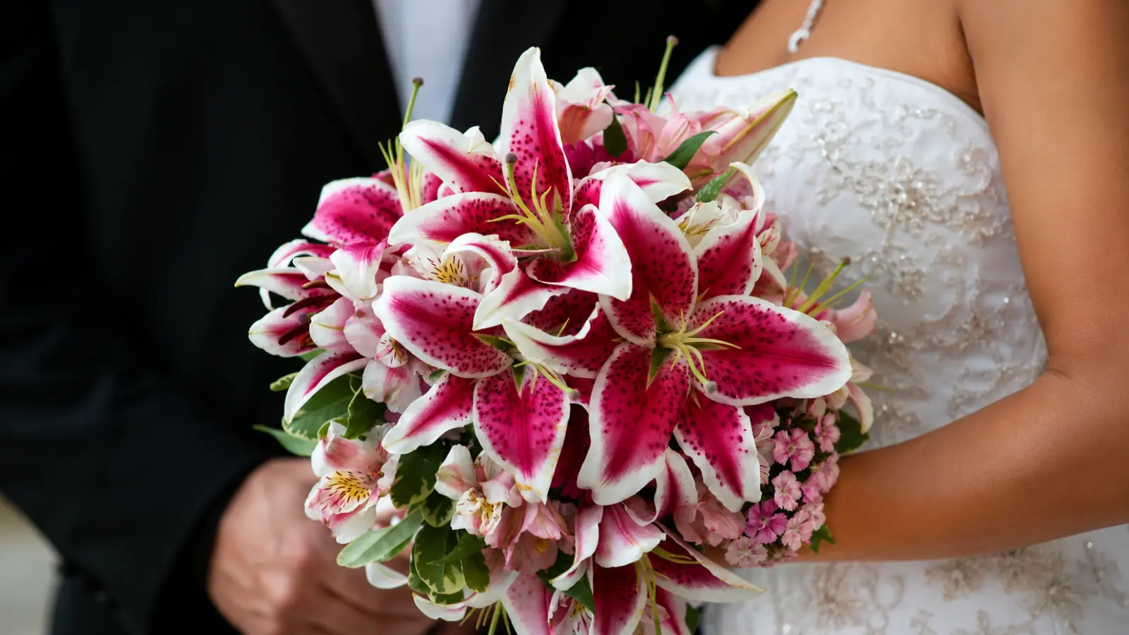 Bride holding a lush bouquet featuring pink Stargazer lilies mixed with delicate pink seasonal flowers
