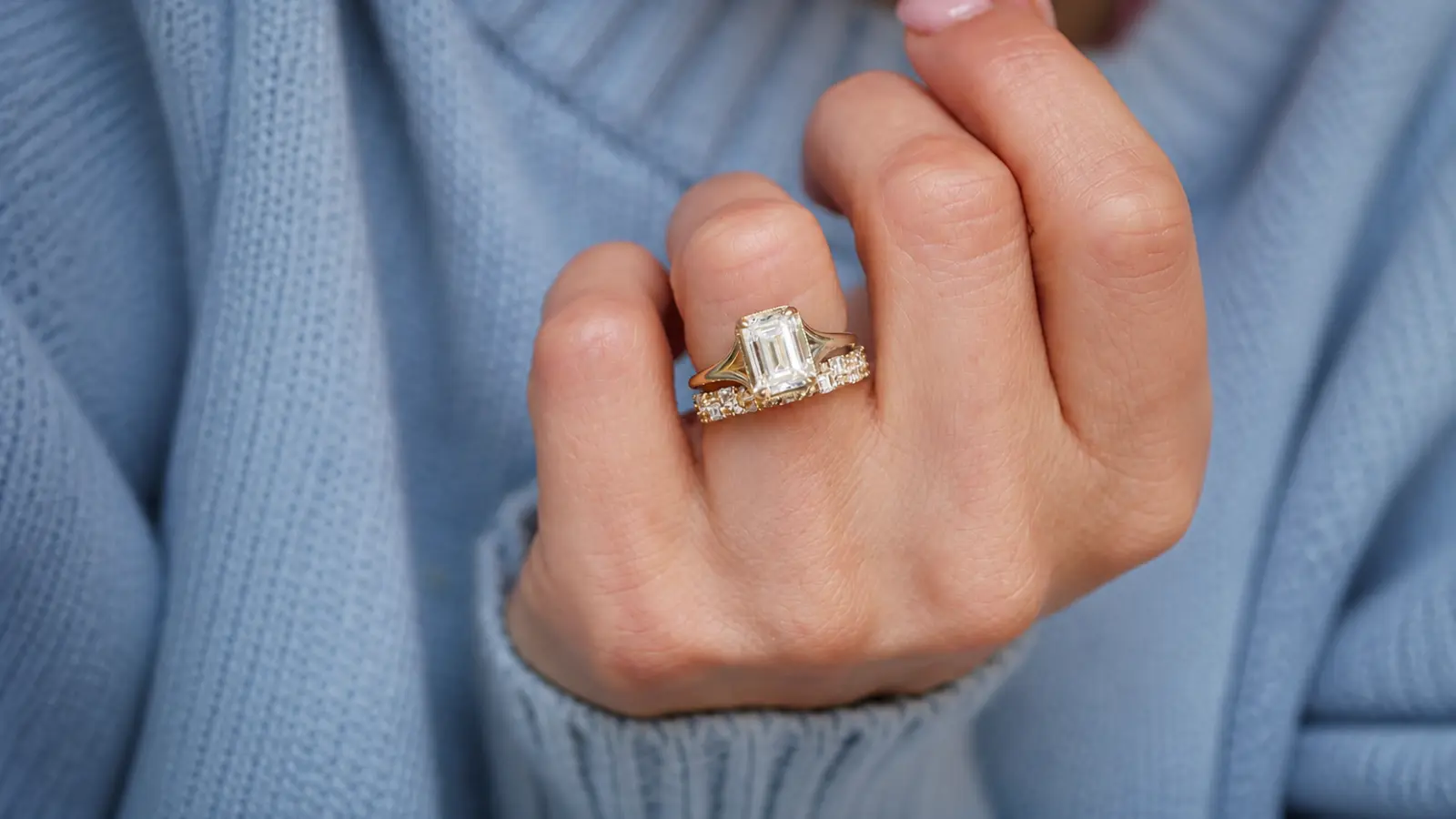 An emerald cut engagement ring paired with a straight diamond wedding band on a woman's hand