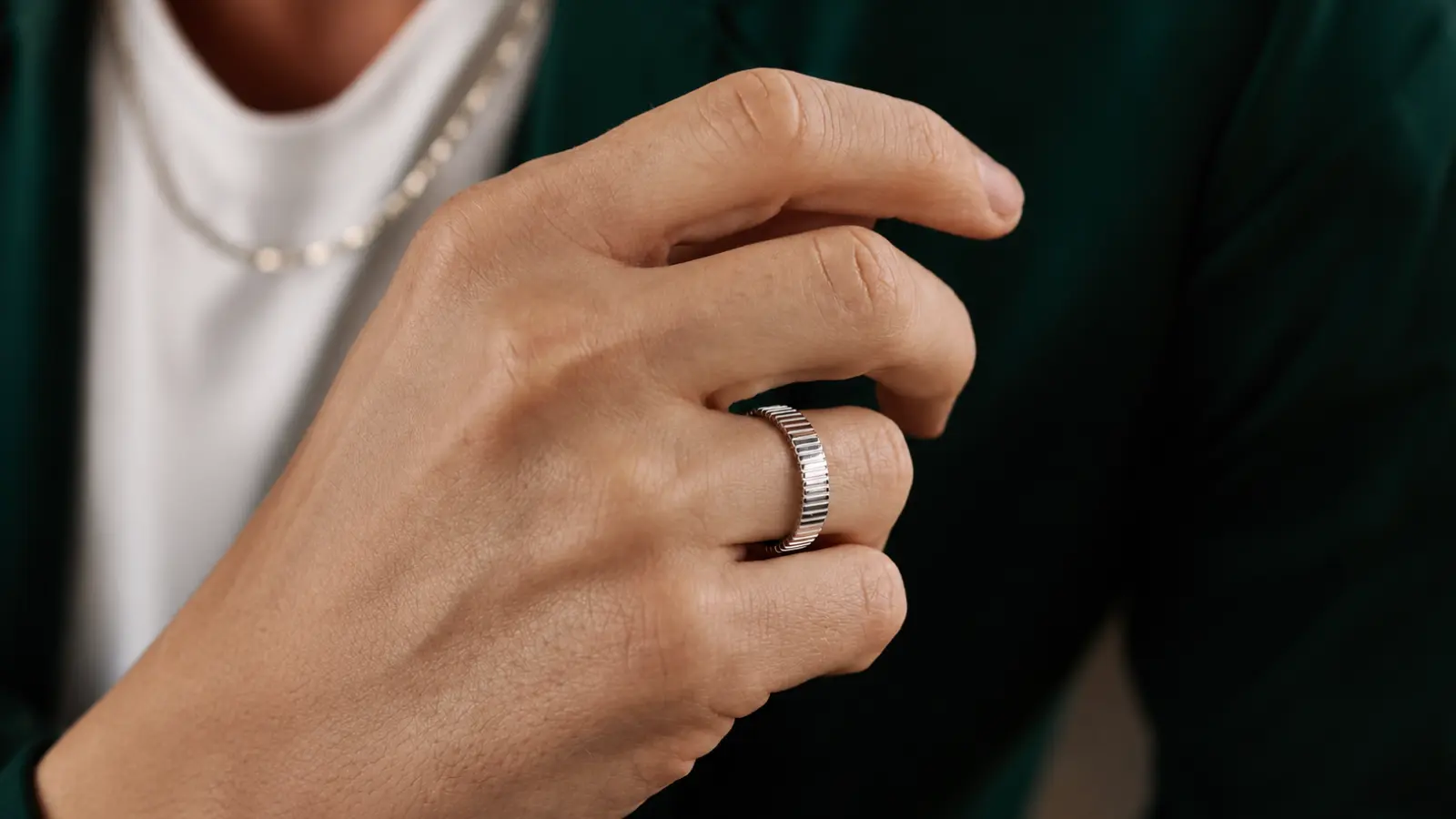 Close-up of a man's hand wearing a textured white gold men's wedding band, emphasizing the modern ridged finish and minimalist design for a refined everyday Men's Wedding Bands