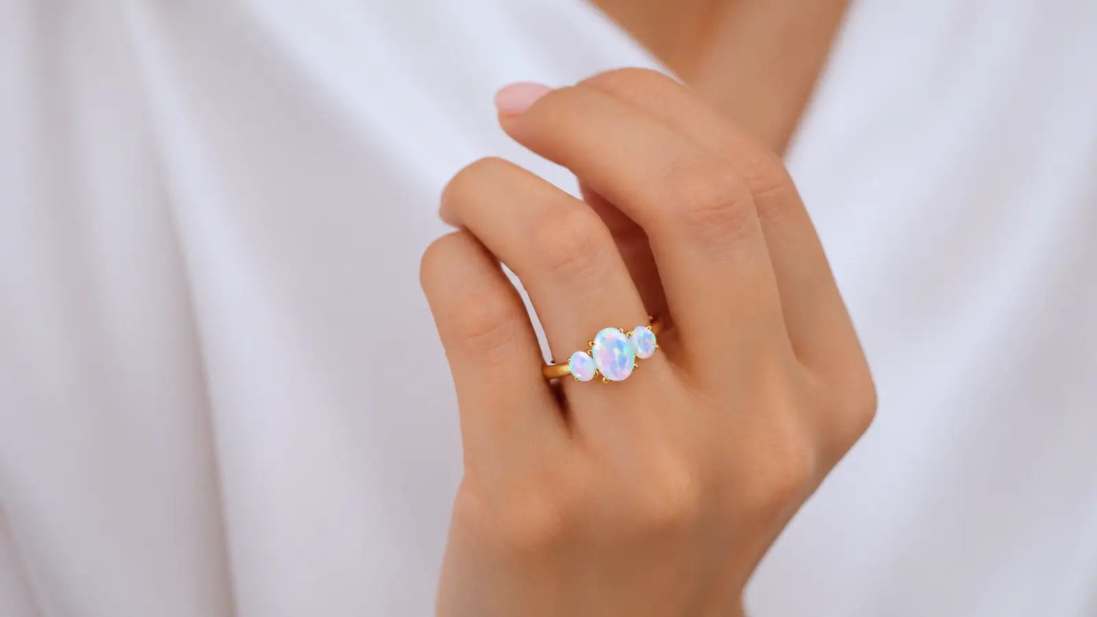 A hand wearing a three-stone opal engagement ring featuring a central oval opal flanked by two smaller opals in a yellow gold setting