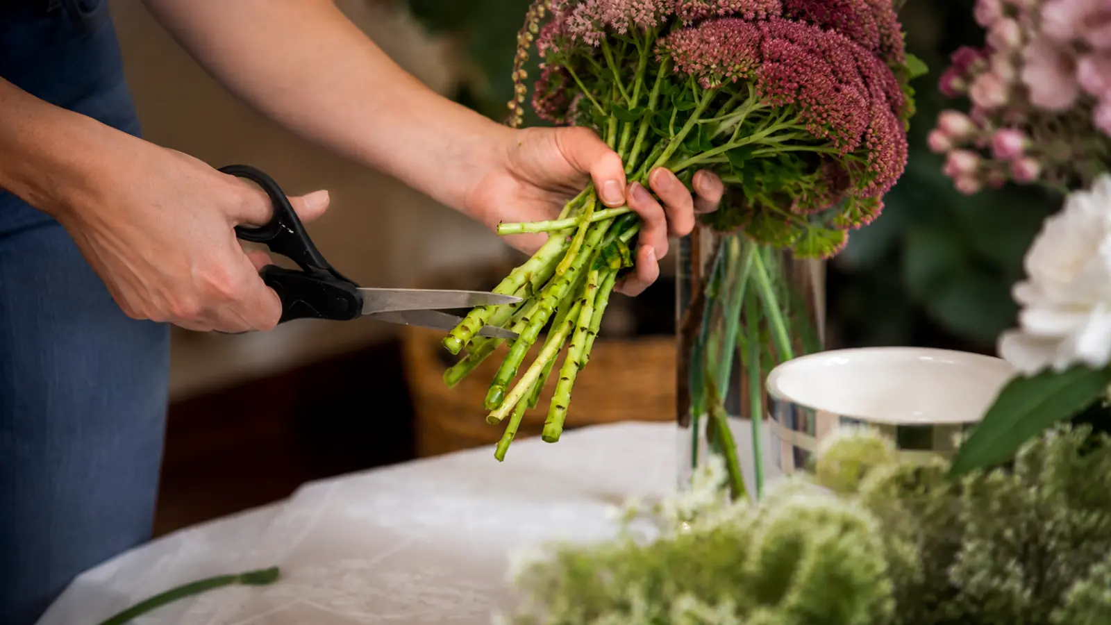 Florist trimming fresh flower stems with floral scissors while preparing a custom wedding bouquet