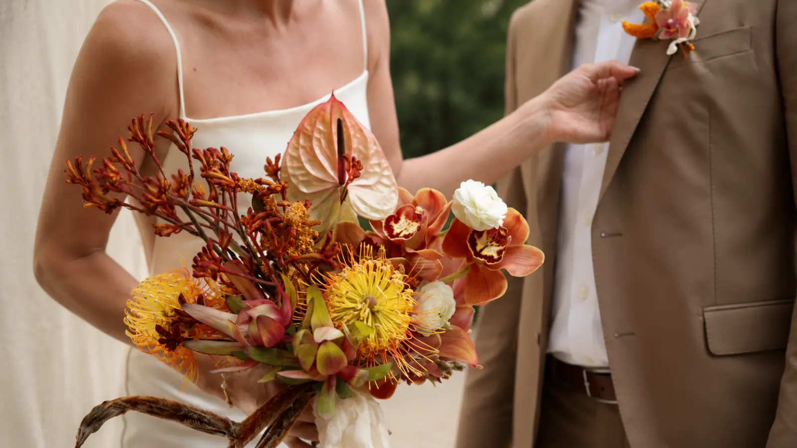Bride holding a tropical fall wedding bouquet with orchids, anthurium, pincushion protea and rich autumn colors