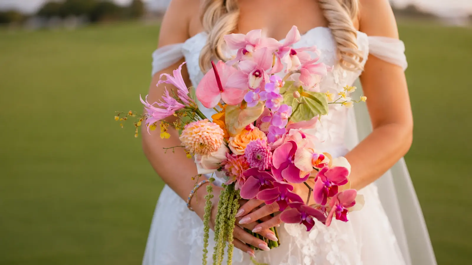 Bride holding a tropical summer wedding bouquet with pink orchids, anthuriums, dahlias and colorful seasonal flowers