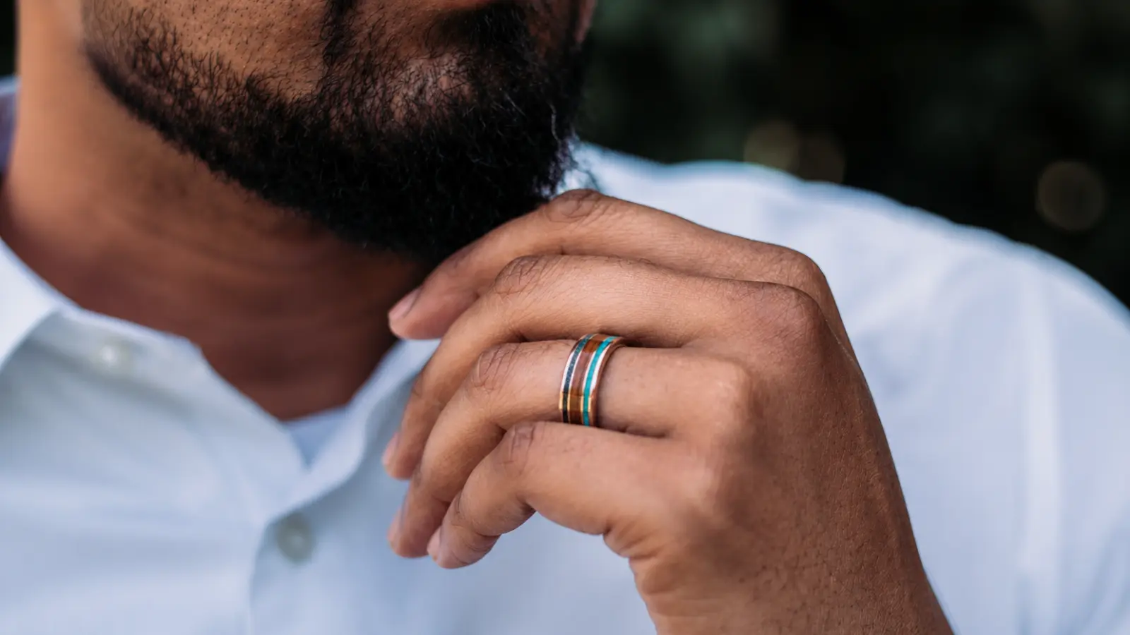 Customer trying on men's wedding bands at a jewelry store while comparing different ring styles with assistance from a jewelry consultant