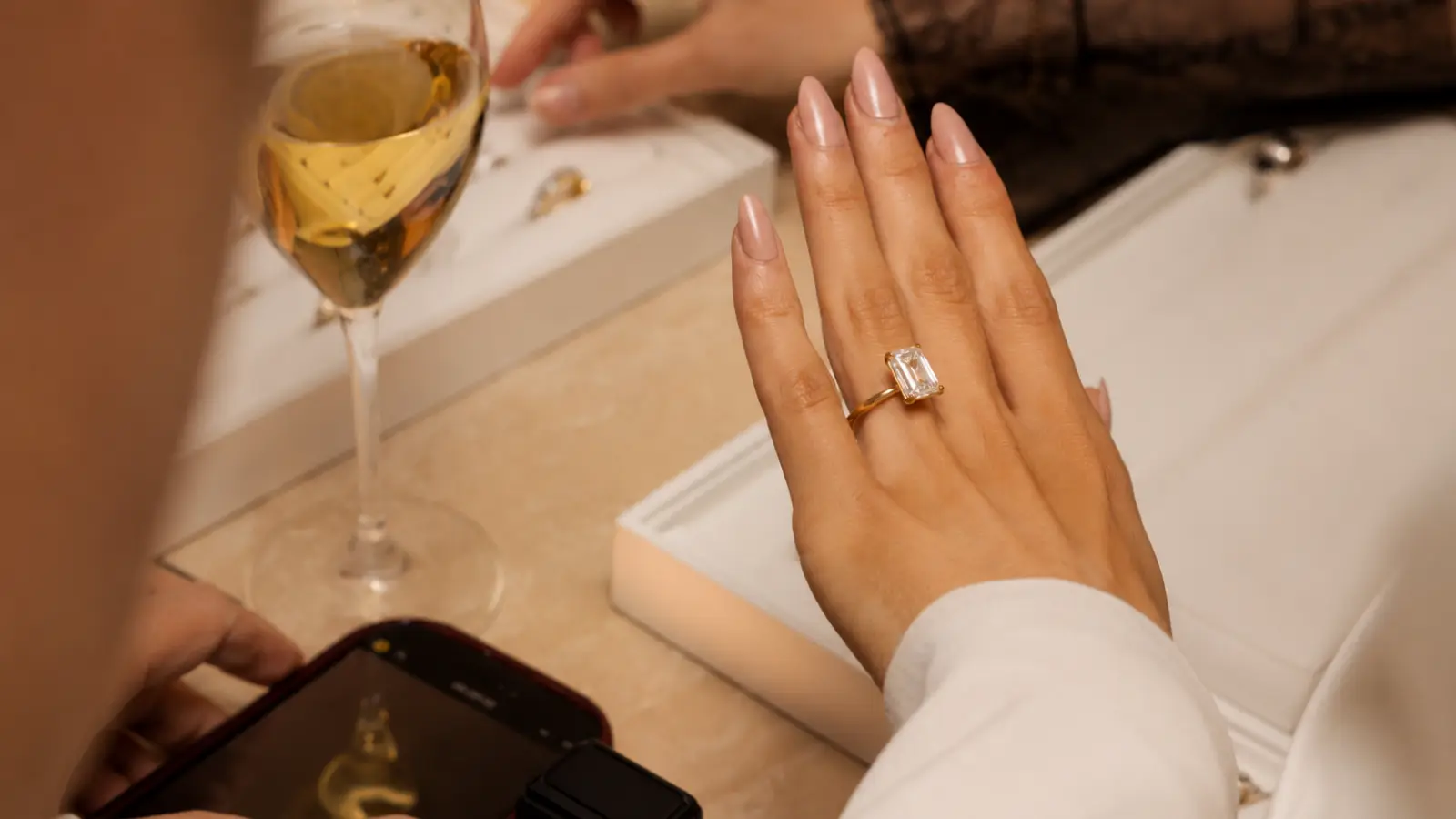 A hand wearing a moissanite engagement ring is photographed inside a jewelry store while comparing different engagement ring styles