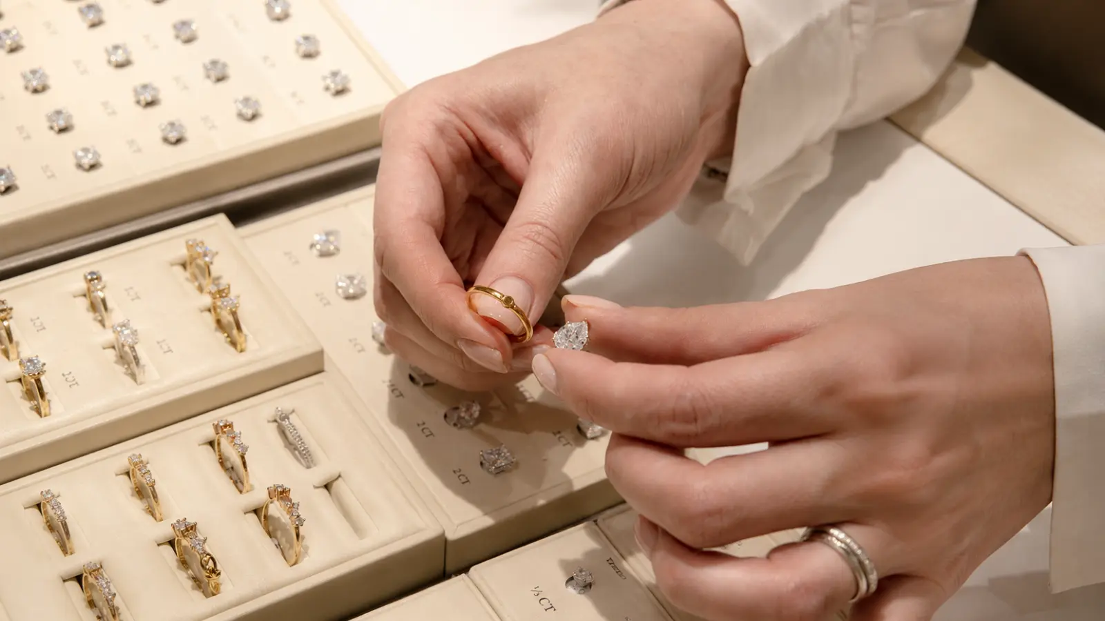 Hands comparing wedding bands with an oval engagement ring inside a jewelry store during the selection process
