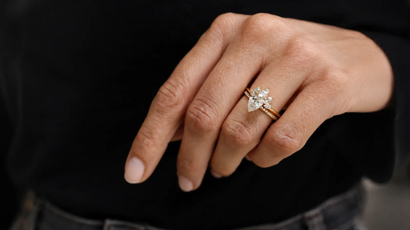 Hands trying different wedding bands with a pear shaped engagement ring inside a jewelry store