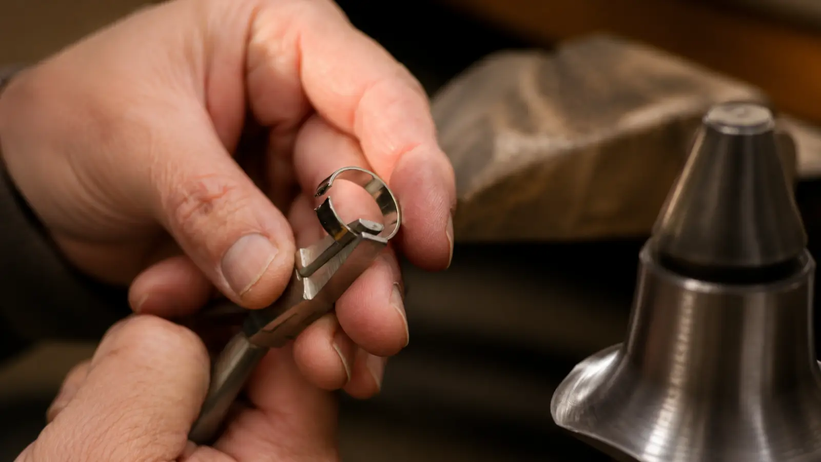 A jeweler holds a tungsten wedding ring with specialized tools, demonstrating why resizing or repairing tungsten bands is significantly more difficult than gold rings