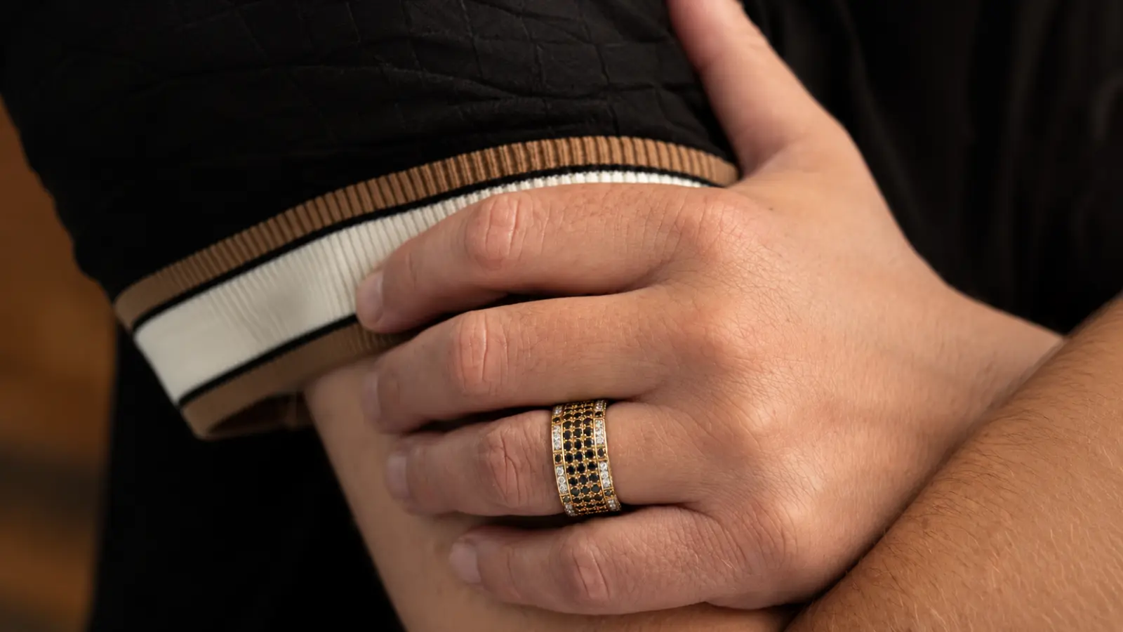 A man's hand wearing a custom black and gold wedding ring with an elegant modern design