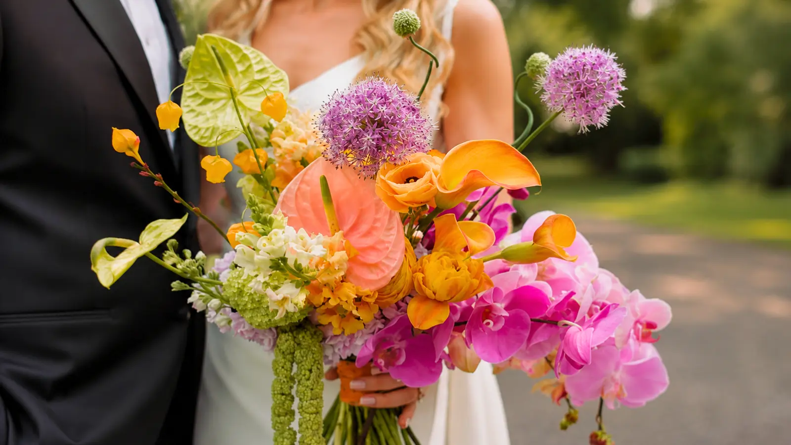 Bride holding a colorful tropical wedding bouquet with orchids, calla lilies, anthuriums and allium flowers