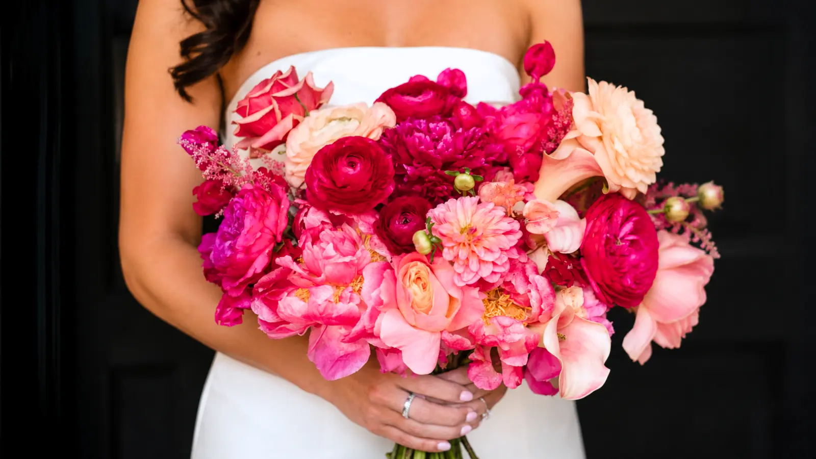 Bride holding a vibrant hot pink wedding bouquet with roses, peonies, ranunculus and calla lilies