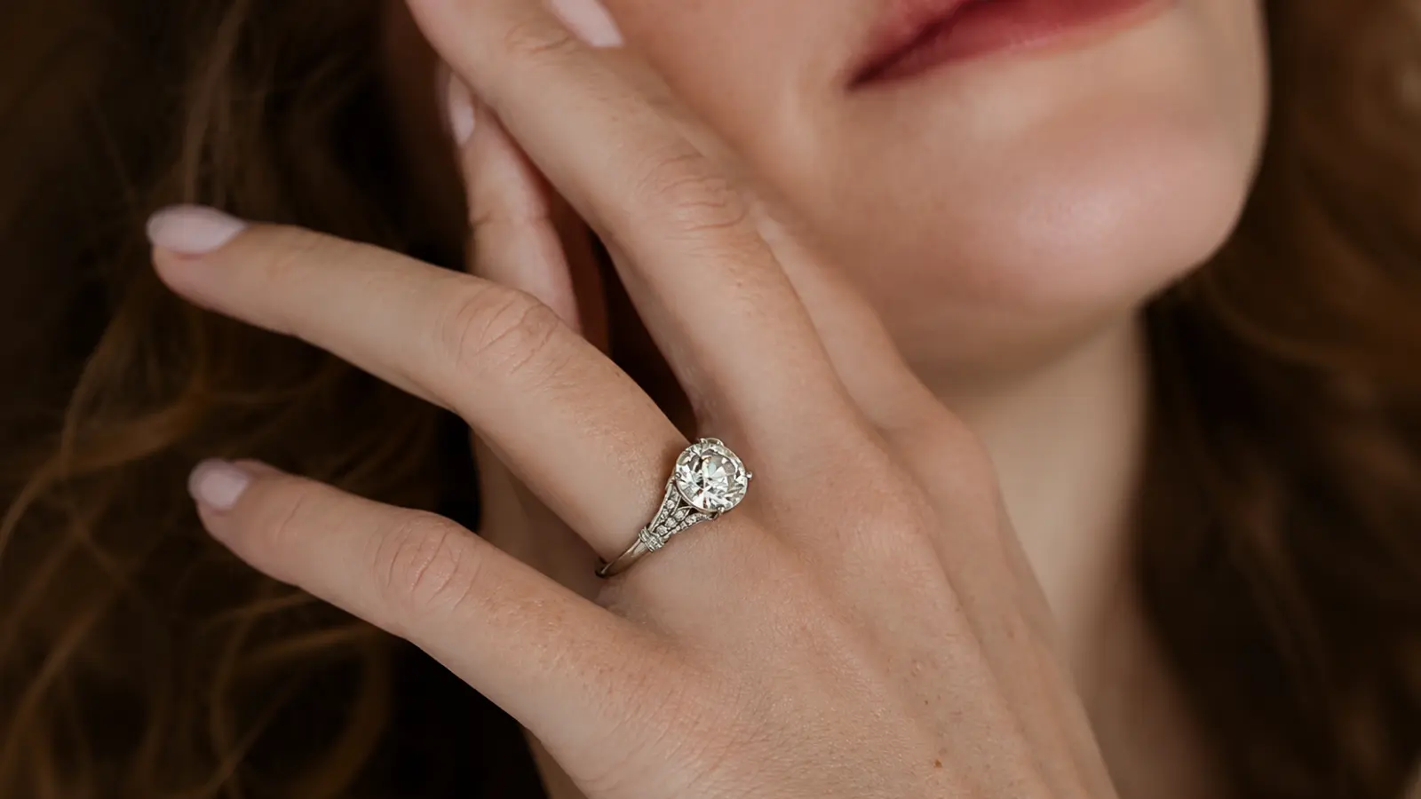 A woman wearing a vintage Art Deco solitaire diamond ring with engraved shoulders and a brilliant round center diamond