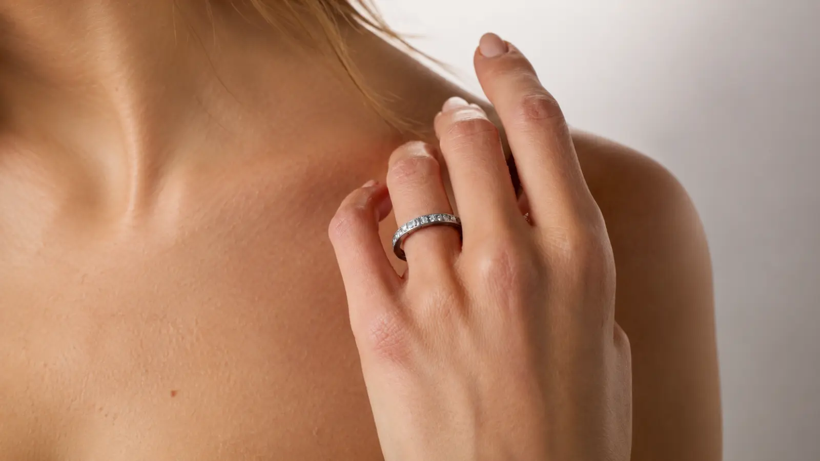 A woman wearing a vintage eternity wedding band with engraved milgrain details while gently touching her shoulder