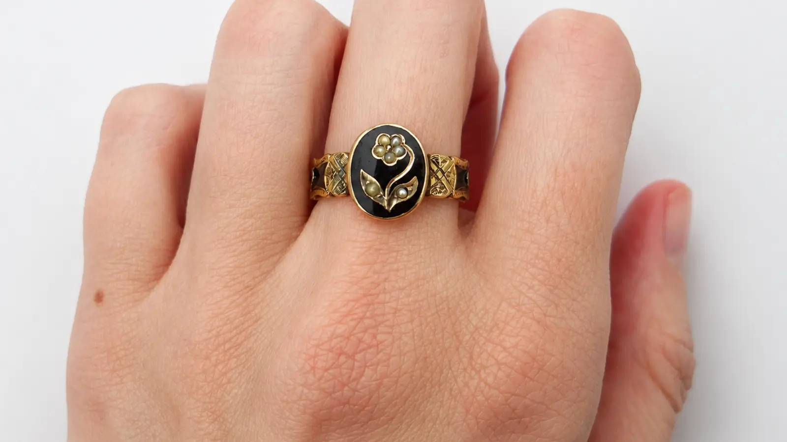 A close-up of a vintage gothic black onyx ring with intricate gold floral details and an oval black centerpiece