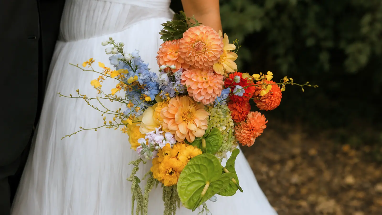 Bride holding a warm color wedding bouquet with peach dahlias, yellow blooms and blue flowers