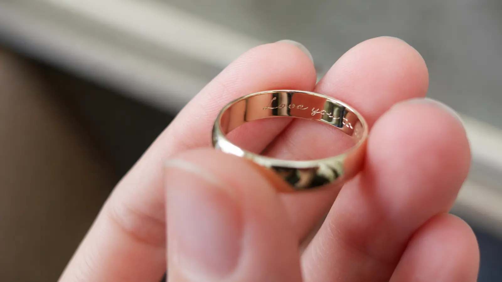 A gold wedding ring featuring a romantic engraved message inside the band held between a person's fingers