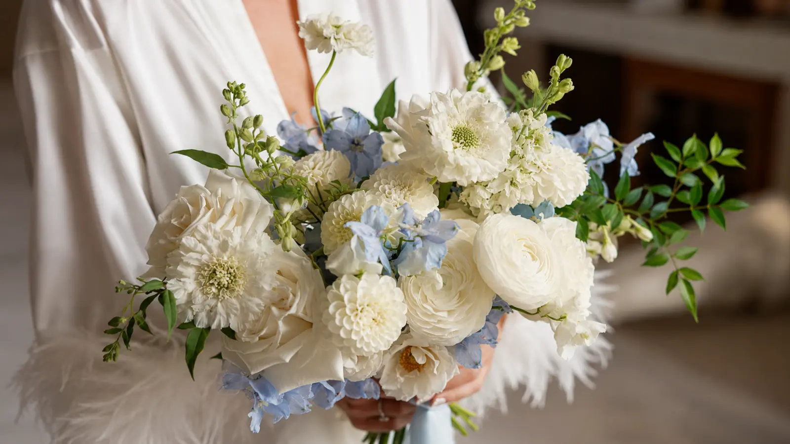 Bride holding a white and dusty blue wedding bouquet with roses, ranunculus and delphinium