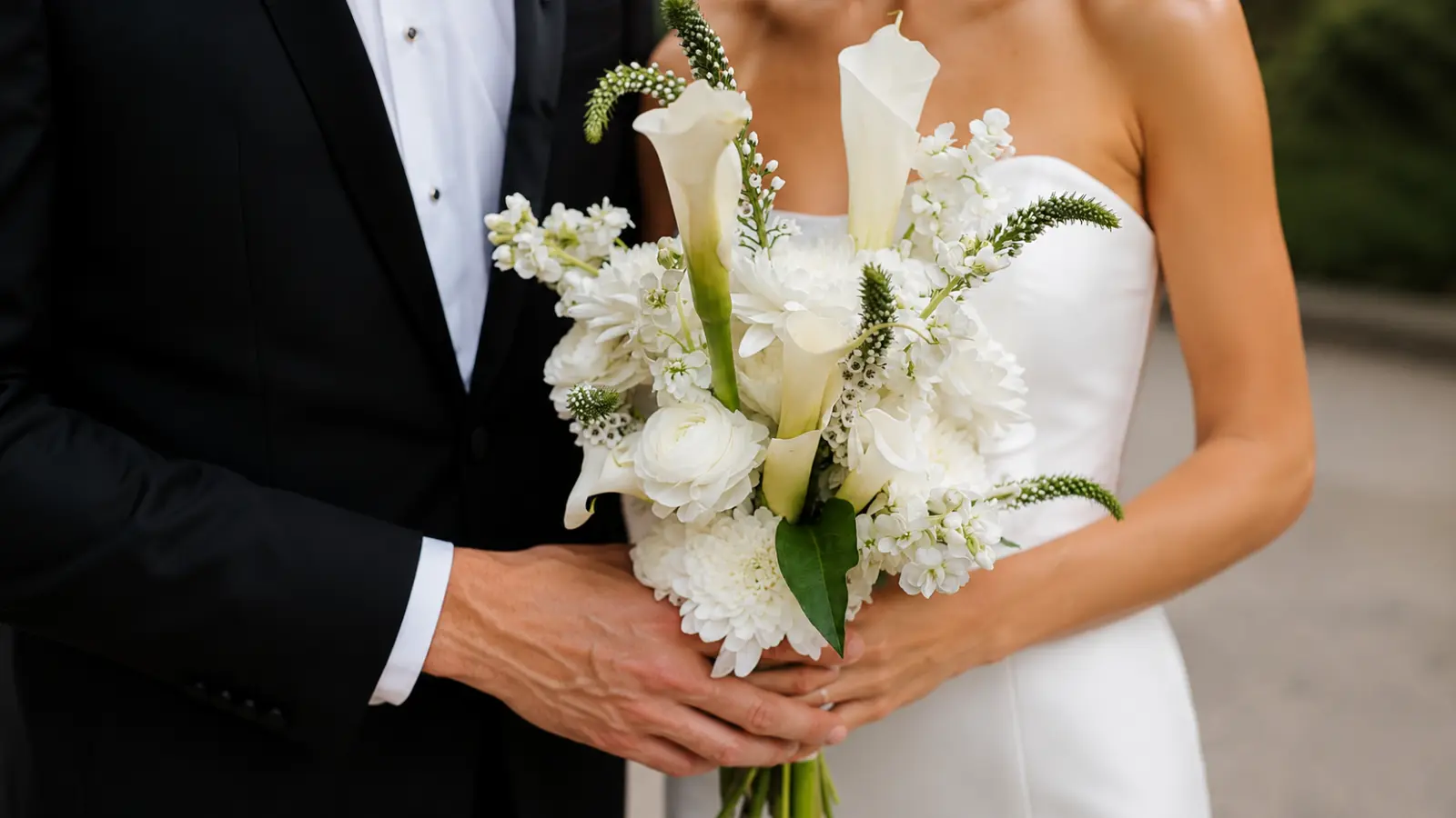 Bride and groom holding a white wedding bouquet with calla lilies and seasonal white flowers