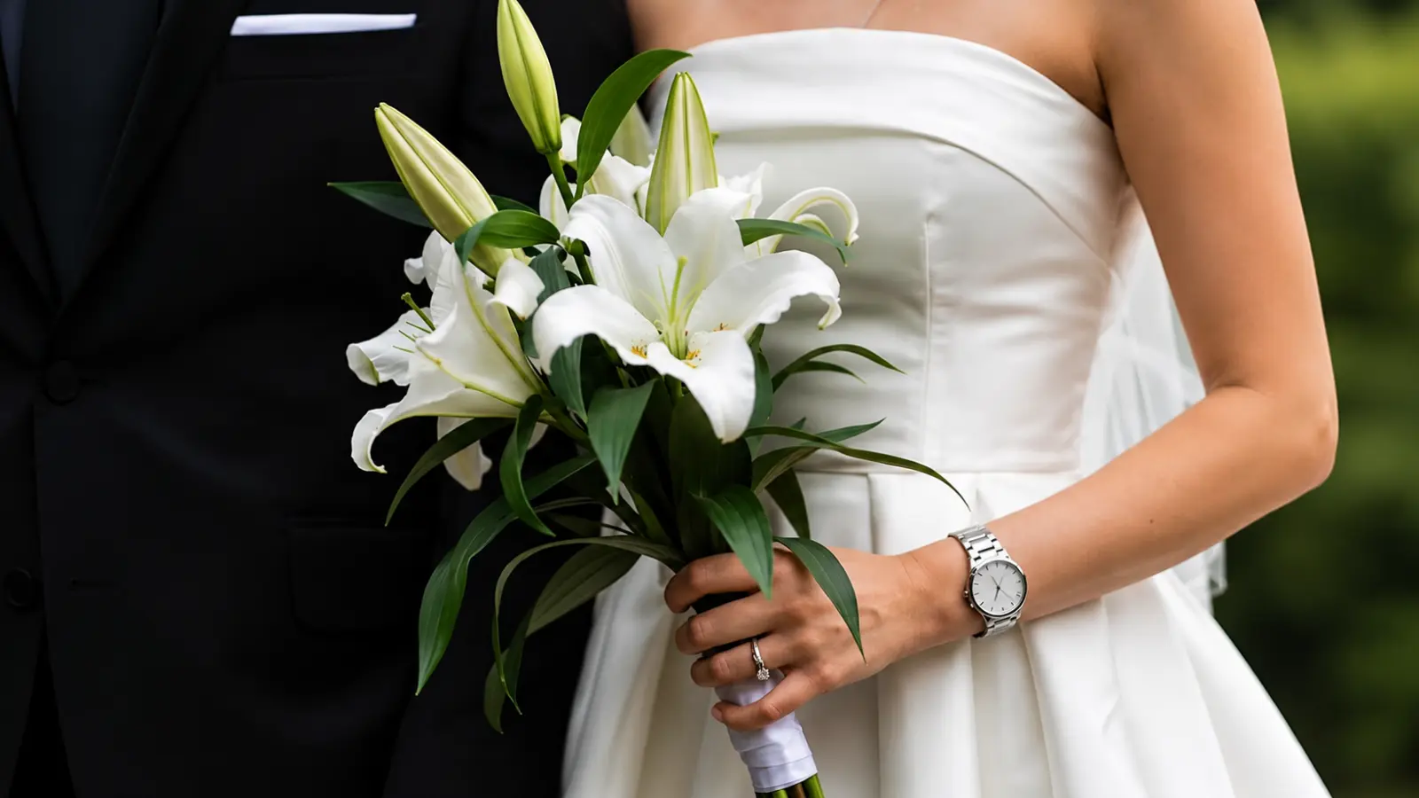 Bride holding a white lily wedding bouquet with fresh green foliage and unopened lily buds