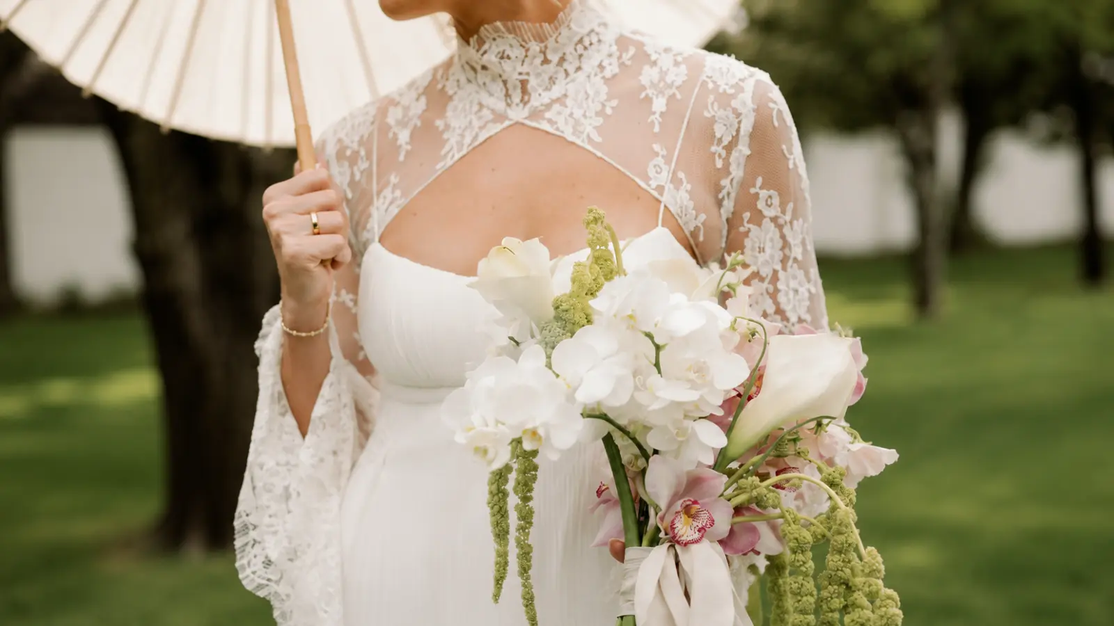 Bride in a lace wedding dress holding a white orchid bridal bouquet with calla lilies and trailing green amaranthus