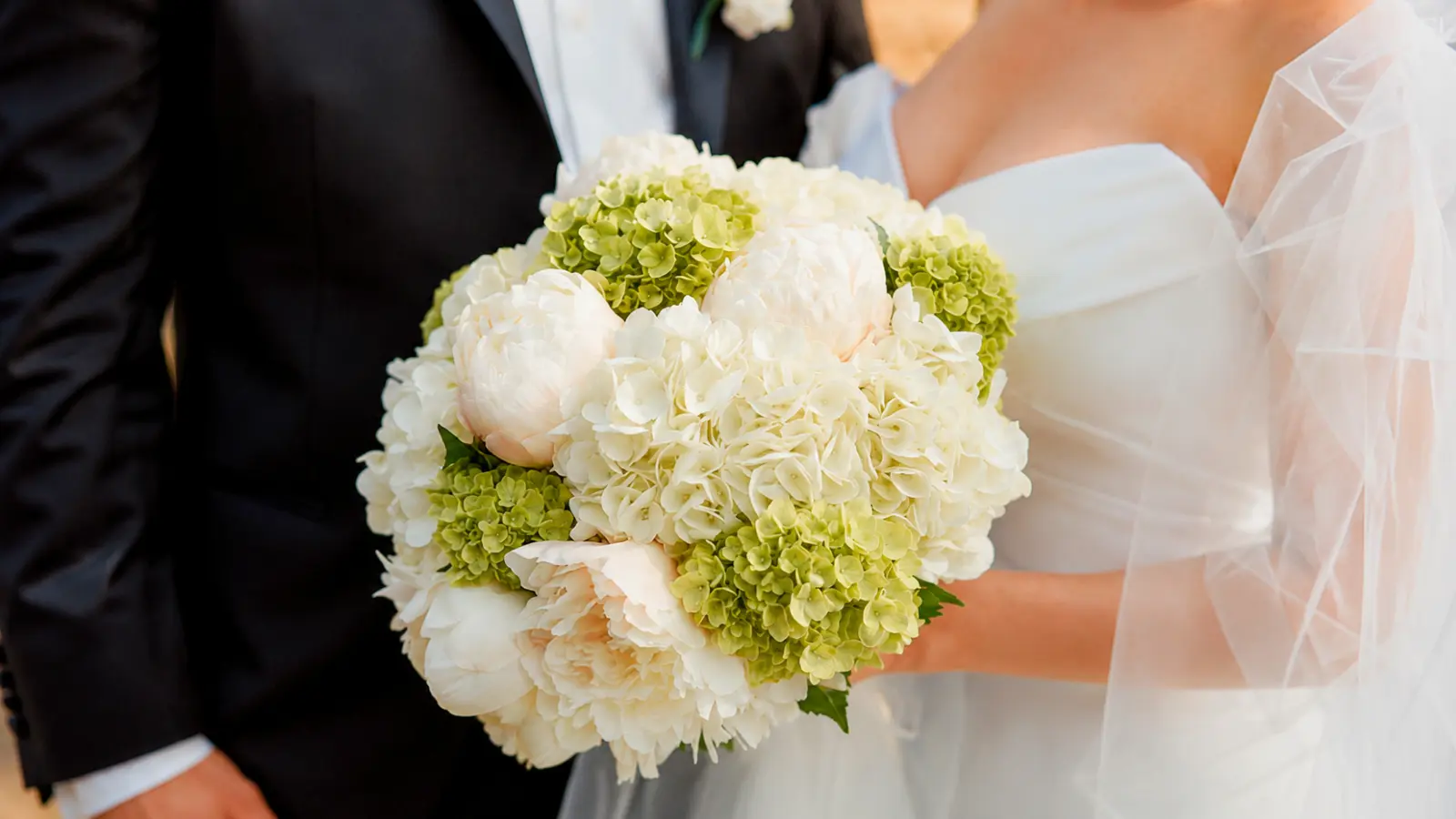 Bride holding a white wedding bouquet featuring white peonies, hydrangeas, and green snowball viburnum flowers