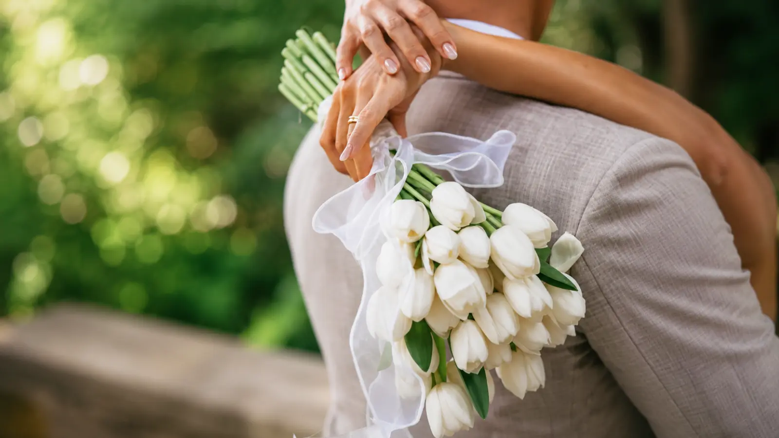 Bride embracing the groom while holding a white tulip wedding bouquet tied with a sheer ribbon