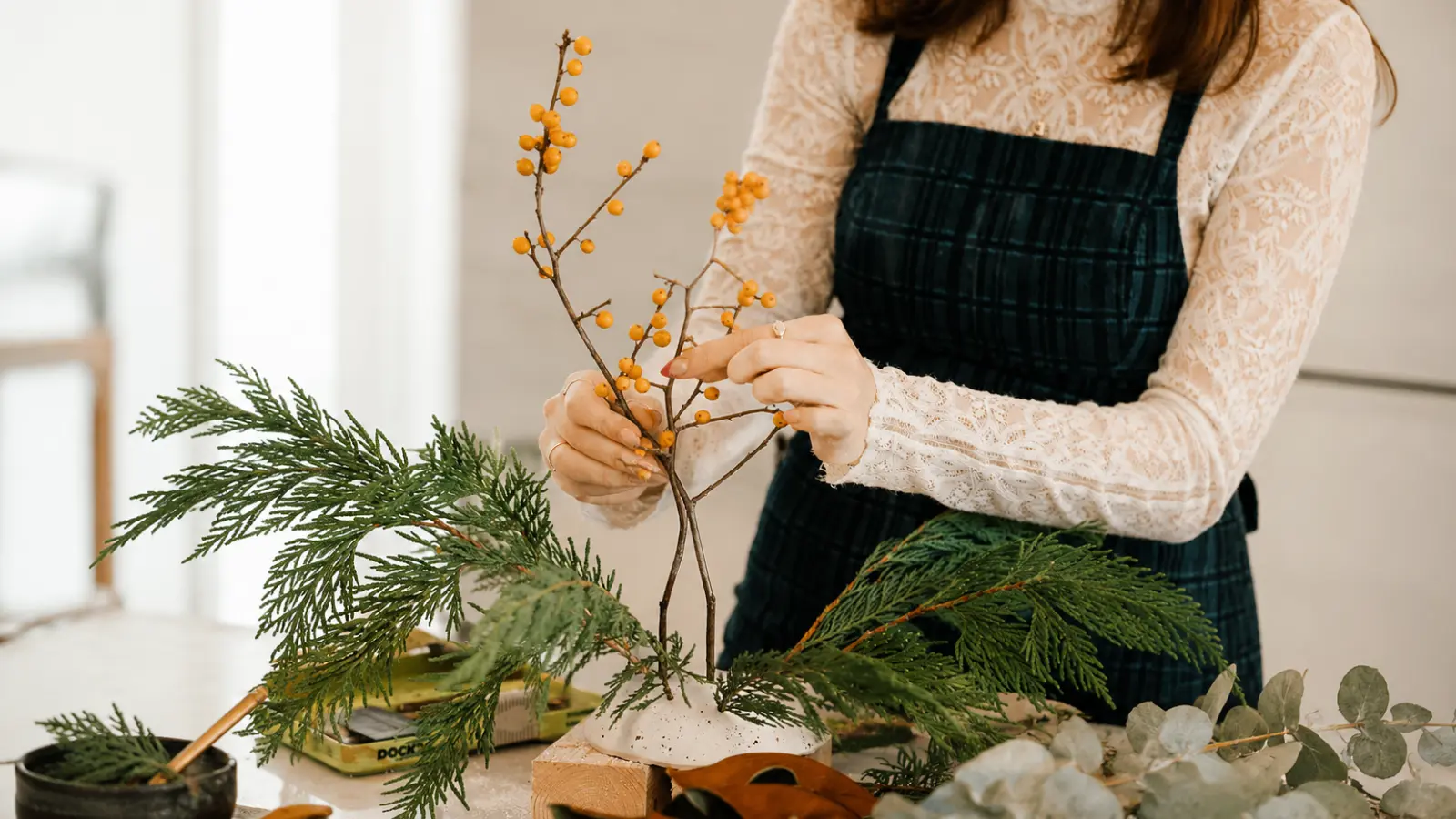 Florist arranging evergreen branches, winter berries and seasonal foliage for a winter wedding bouquet