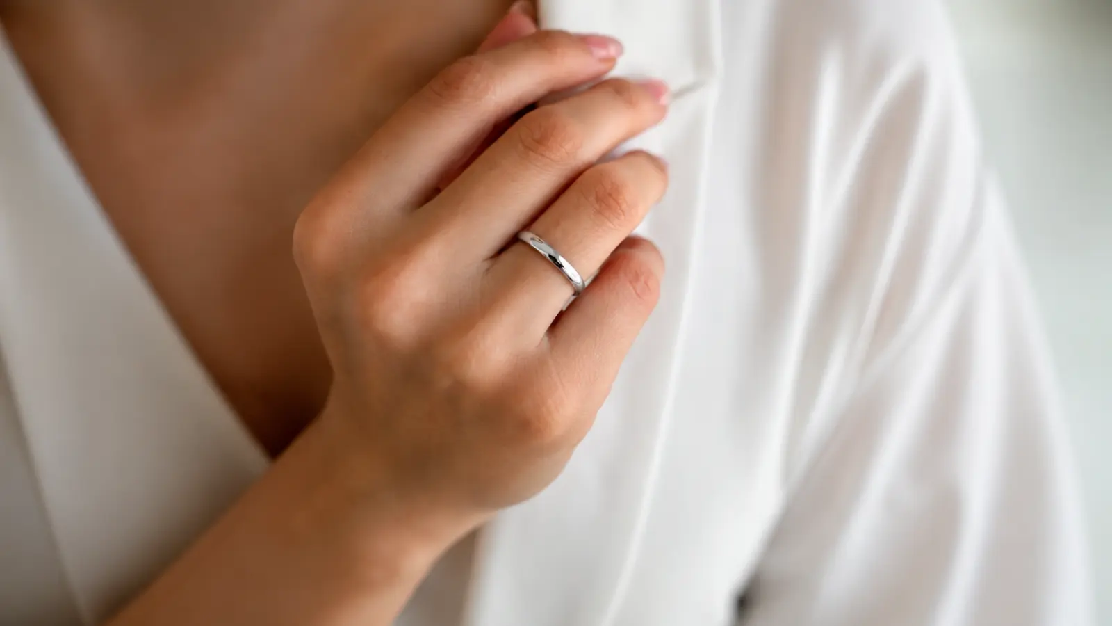 A close-up of a woman wearing a polished platinum wedding ring, highlighting the naturally white metal, elegant simplicity and comfortable everyday design of a classic band