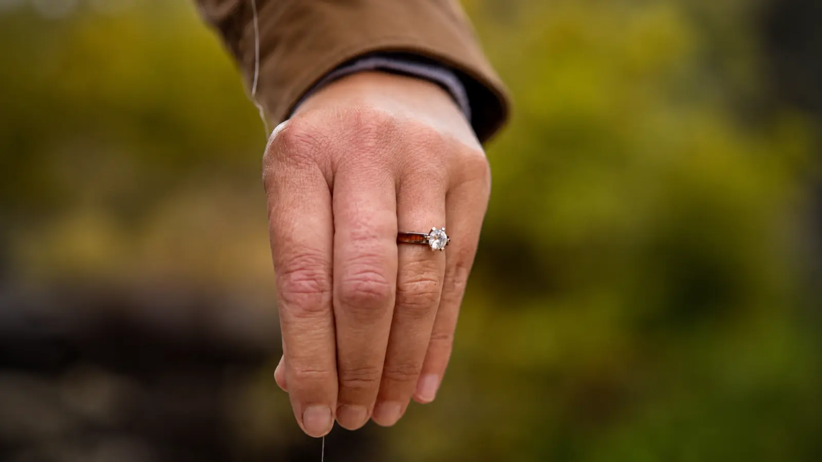 A hand wearing a wood engagement ring is shown outdoors, highlighting the natural wood band paired with a classic solitaire diamond