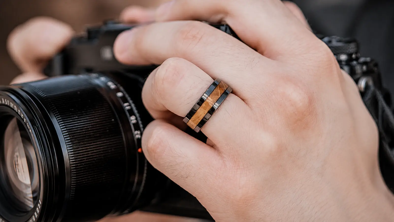 A close-up of a hand wearing a wood inlay wedding ring while holding a camera, highlighting the blend of natural wood and contemporary design