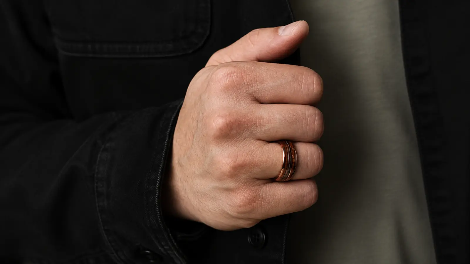 A hand wearing a polished wood wedding ring displays the natural grain pattern and handcrafted design with a warm rustic aesthetic