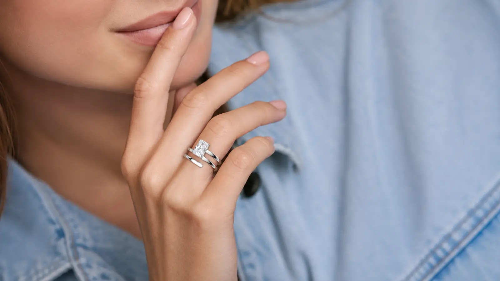 A woman wearing a white gold wrap style engagement ring enhancer surrounding a princess-cut diamond solitaire