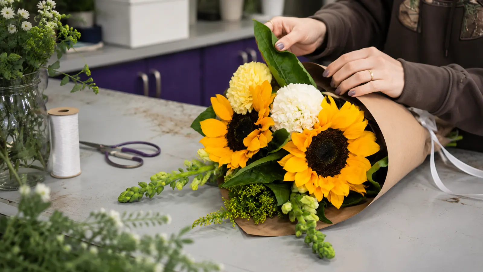 Florist wrapping a sunflower wedding bouquet with fresh flowers and greenery