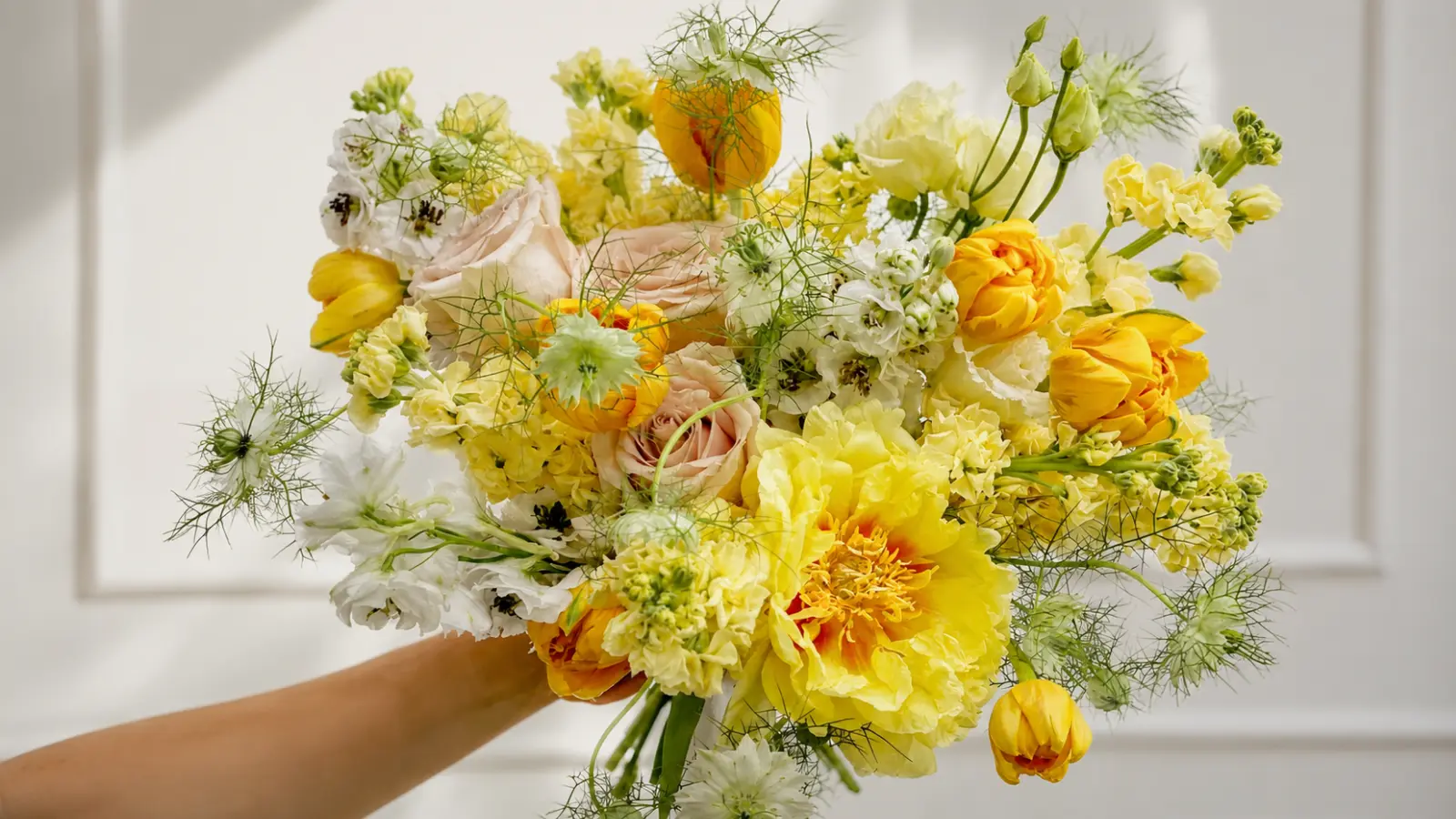 Hand holding a yellow and white colorful wedding bouquet with tulips, daffodils and delicate spring flowers