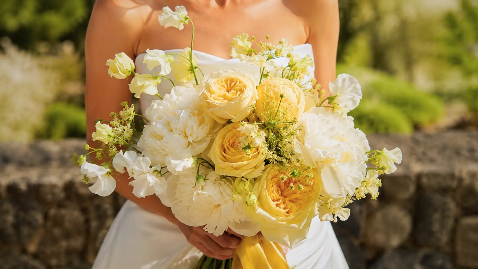 Bride holding a yellow and white wedding bouquet with peonies and garden roses