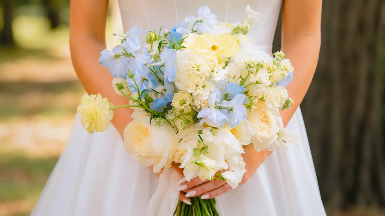Bride holding a yellow blue and white wedding bouquet with delphiniums and white roses