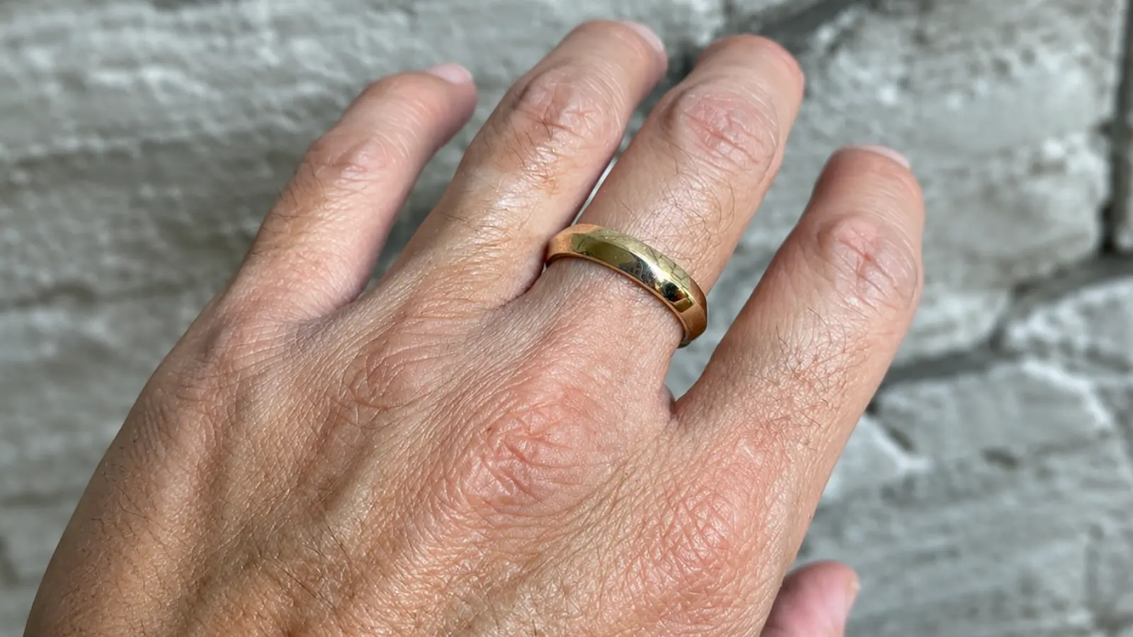 Detailed close-up of a hand wearing a polished yellow gold men's wedding band against a textured stone background