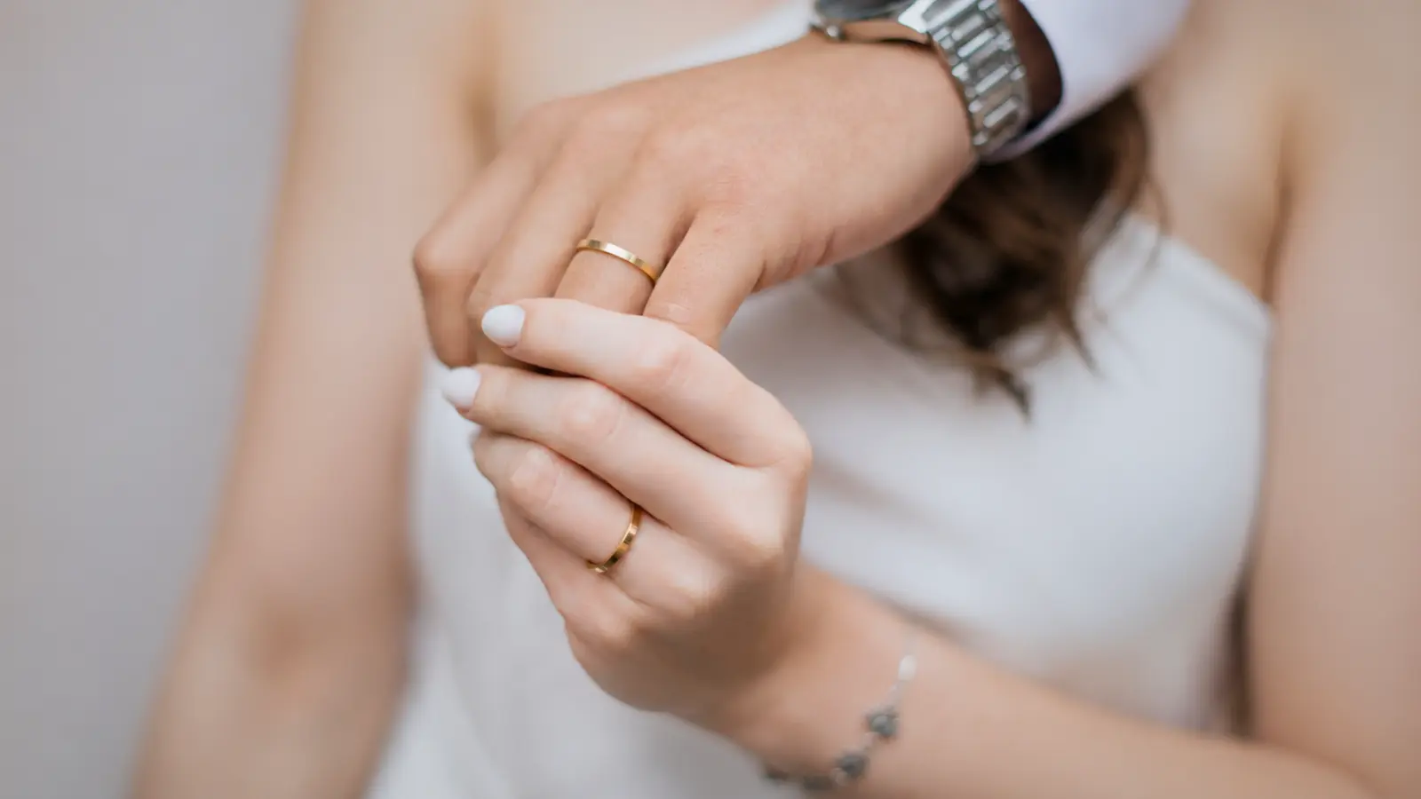 A bride gently holds the groom's hand while both wear polished yellow gold wedding rings, highlighting classic matching bands that offer a timeless and elegant wedding jewelry style