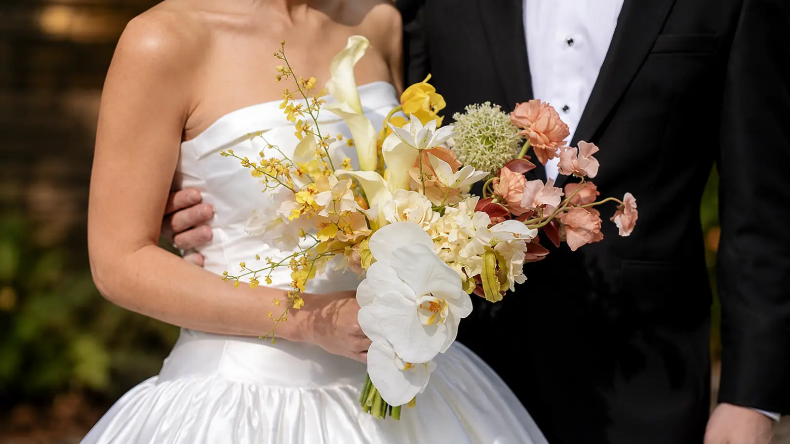 Bride and groom holding a yellow orchid wedding bouquet with calla lilies, peach flowers, and soft garden-inspired accents