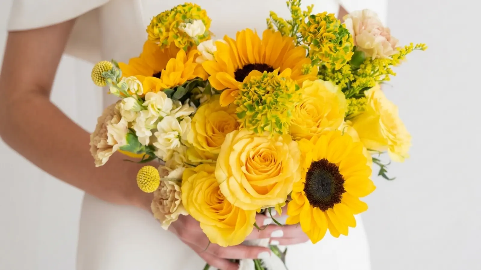 Bride holding a sunflower wedding bouquet with yellow roses, carnations, and fresh seasonal flowers