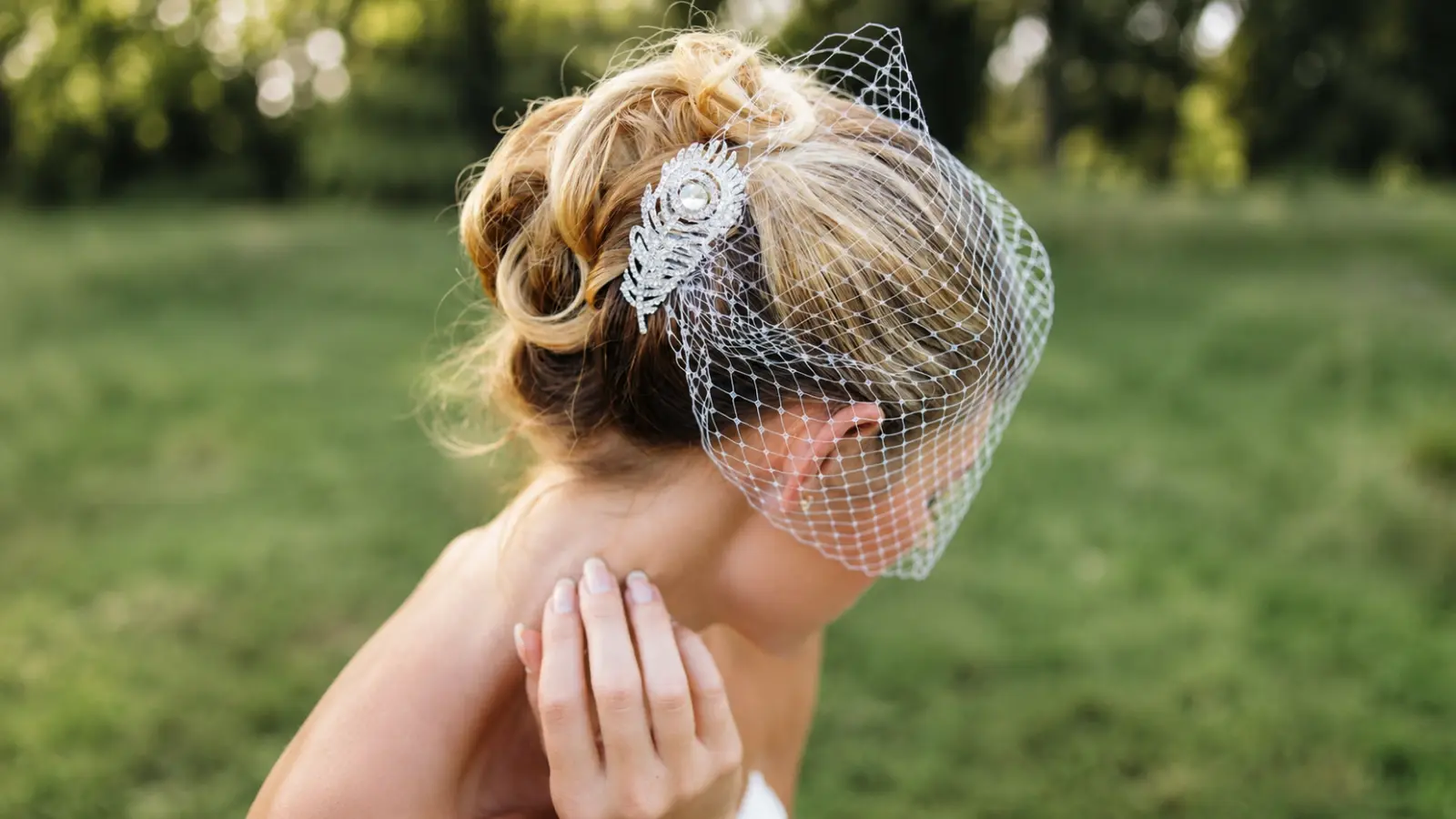 Bride wearing a white birdcage wedding veil across her face with a sparkling jeweled hair comb securing her curled bridal updo Birdcage Wedding Veil