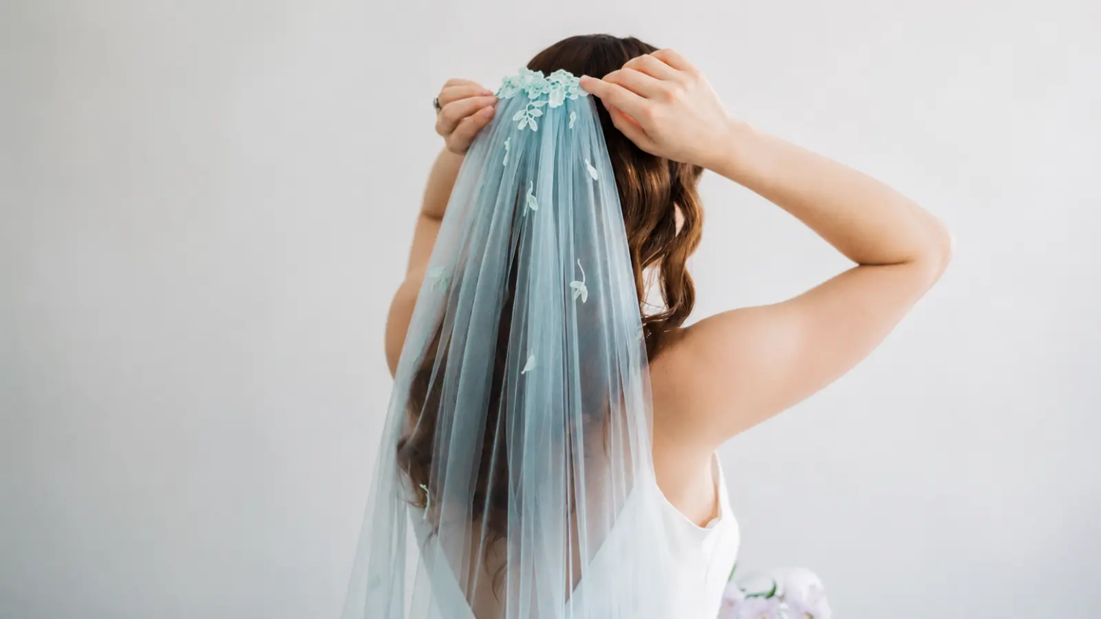 Bride adjusting a blue colored wedding veil with sheer tulle and delicate floral lace details attached near the crown