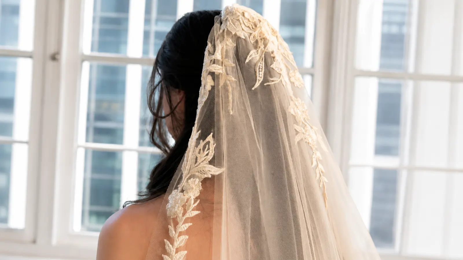 Bride wearing a champagne colored wedding veil with sheer tulle and dimensional floral lace appliqués illuminated by natural window light