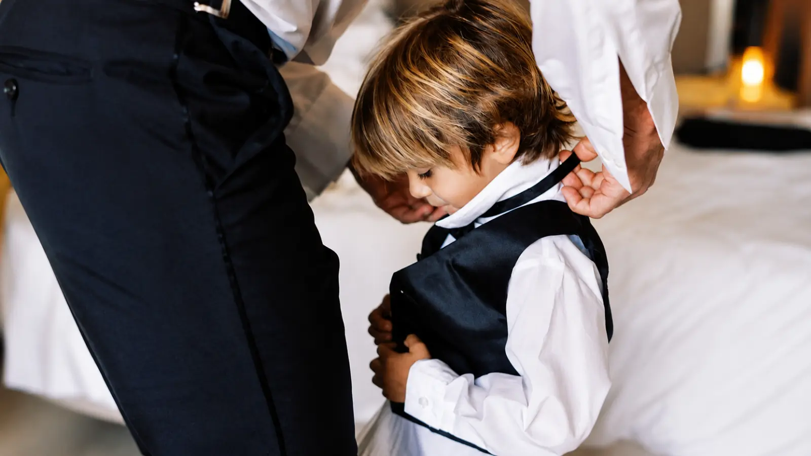 Young boy dressed in formal wedding attire while an adult adjusts his tie, showing the getting-ready process for children attending or participating in weddings