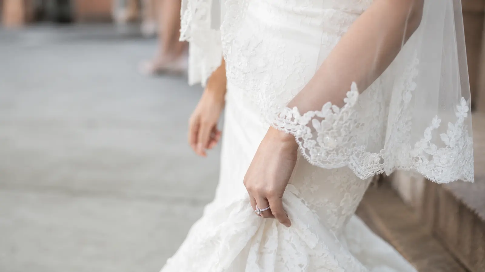 Bride wears a fingertip wedding veil with an ornate lace border falling near her hands and coordinating with her lace wedding gown