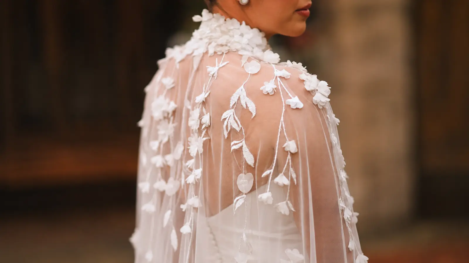 Bride wearing a sheer white floral bridal cape with dimensional appliqués as an elegant alternative to a traditional wedding veil