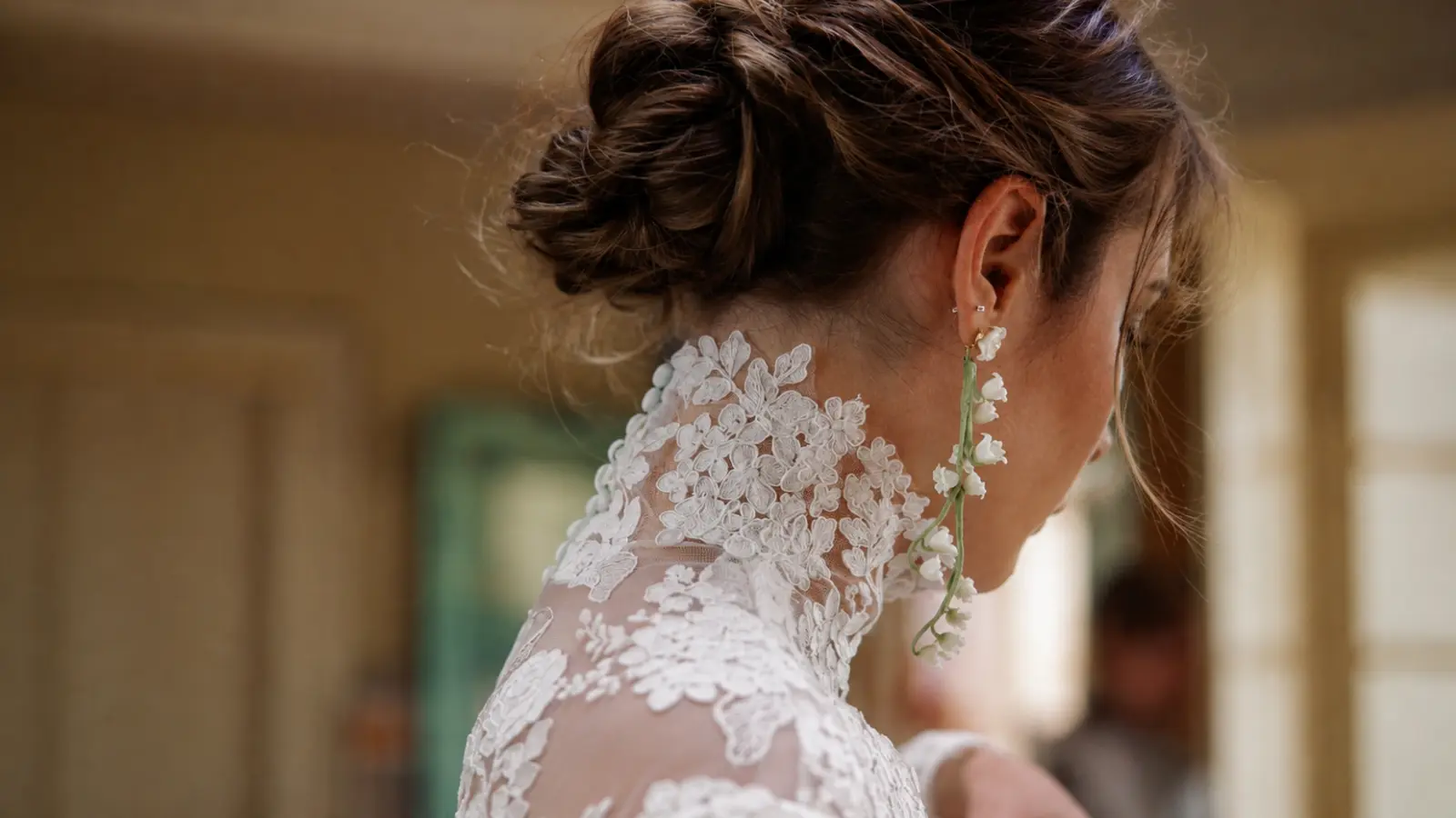 Bride with an intricate updo wearing long white floral statement earrings as a delicate accessory alternative to a wedding veil