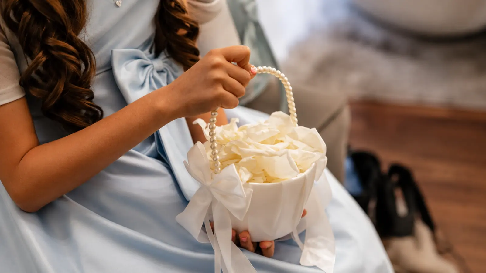 lower girl basket with white flower petals, pearl handle, and white ribbon bow held by a girl wearing a light blue formal dress