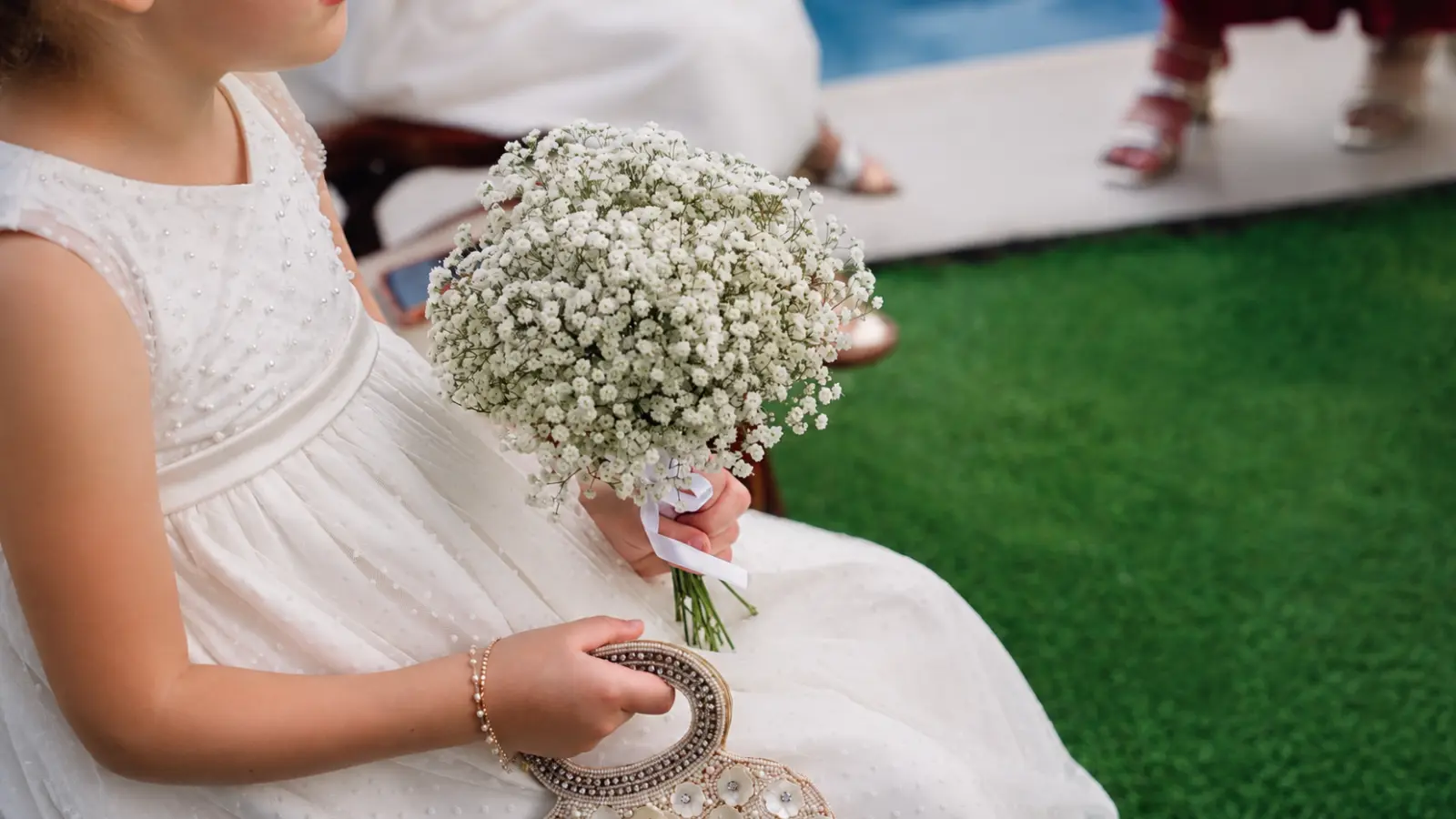 Flower girl duties at the ceremony with a young girl wearing a white dress and holding a bouquet of white baby’s breath flowers